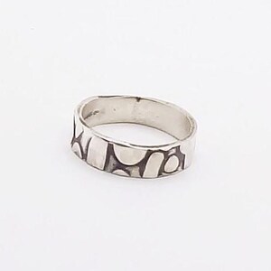 Puede incluir: Un anillo de plata con un diseño abstracto texturizado. El anillo es ancho y tiene un acabado liso y pulido.