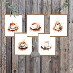 May include: A collection of five watercolor art prints featuring coffee cups on saucers. Each print showcases a different coffee cup design with steam rising, set against a white background and a brown border. The prints are arranged on a wooden background.