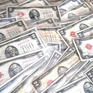 May include: A close-up image of a stack of vintage two dollar bills in protective plastic sleeves. The bills are in various states of wear and tear, with some showing signs of age and use. The bills feature a portrait of Thomas Jefferson and the words "Two Dollars" printed in black ink.