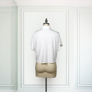 May include: White short-sleeved blouse with a ruffled collar. The blouse is on a white mannequin against a white background.