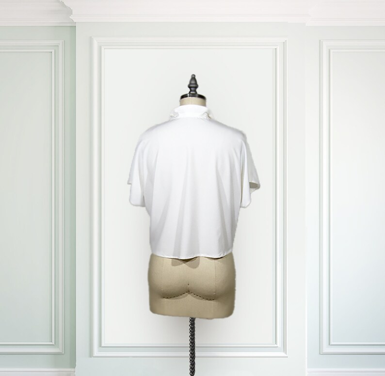 May include: White short-sleeved blouse with a ruffled collar. The blouse is on a white mannequin against a white background.