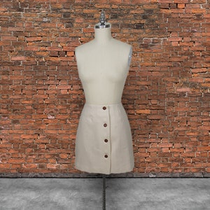 May include: A cream-colored skirt with a button-up front and a slightly A-line silhouette. The skirt is made of a textured fabric and has a casual, relaxed look.