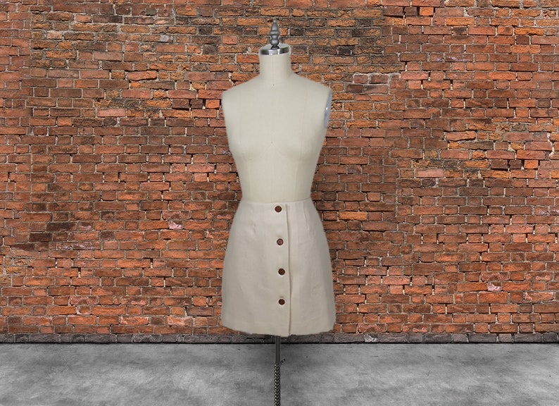 May include: A cream-colored skirt with a button-up front and a slightly A-line silhouette. The skirt is made of a textured fabric and has a casual, relaxed look.