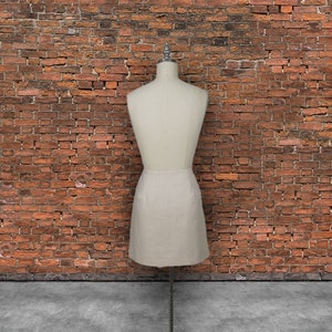 May include: A white skirt on a dress form in front of a brick wall.
