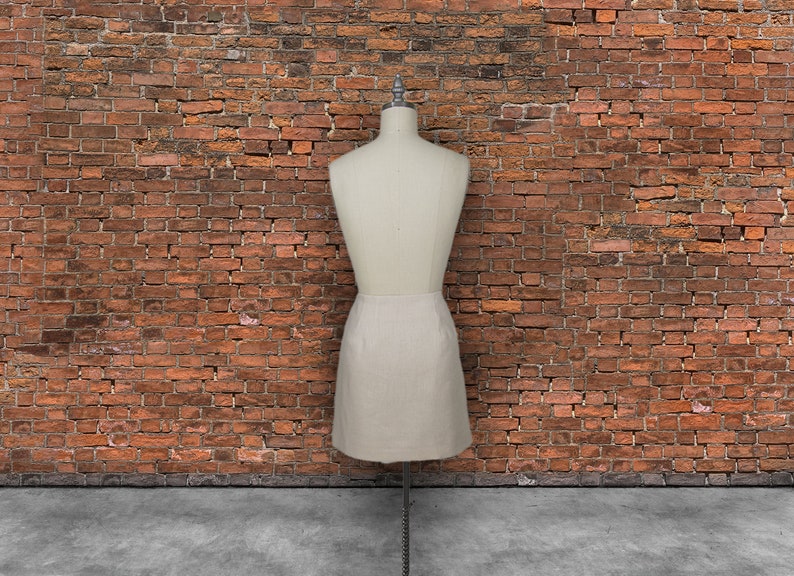 May include: A white skirt on a dress form in front of a brick wall.