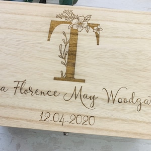 May include: A wooden keepsake box with a floral design and the letter "T" engraved on the lid. The box is personalized with the name "Tia Florence May Woodgate" and the date "12-04-2020".