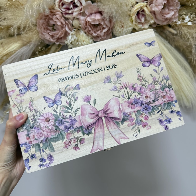 May include: Wooden keepsake box with a floral and butterfly design. The box features a large pink bow and the name "Lola Mary Mahon" along with the date, time, and weight. The box is decorated with purple and pink flowers and butterflies.