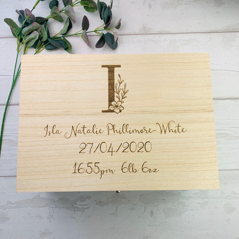 May include: A light wood keepsake box with a floral design and the letter "I" engraved on the lid. The box also has the text "Isla Natalie Phillimore-White 27/04/2020 16:55pm 6lbs 6oz" engraved on the lid.