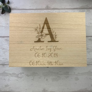 May include: A wooden keepsake box with an engraved floral design and the letter A. The box is personalized with the name Amelia Ivy Glens, the date 06-10-2018, and the time 06:10 am, 8 lbs 10 oz.