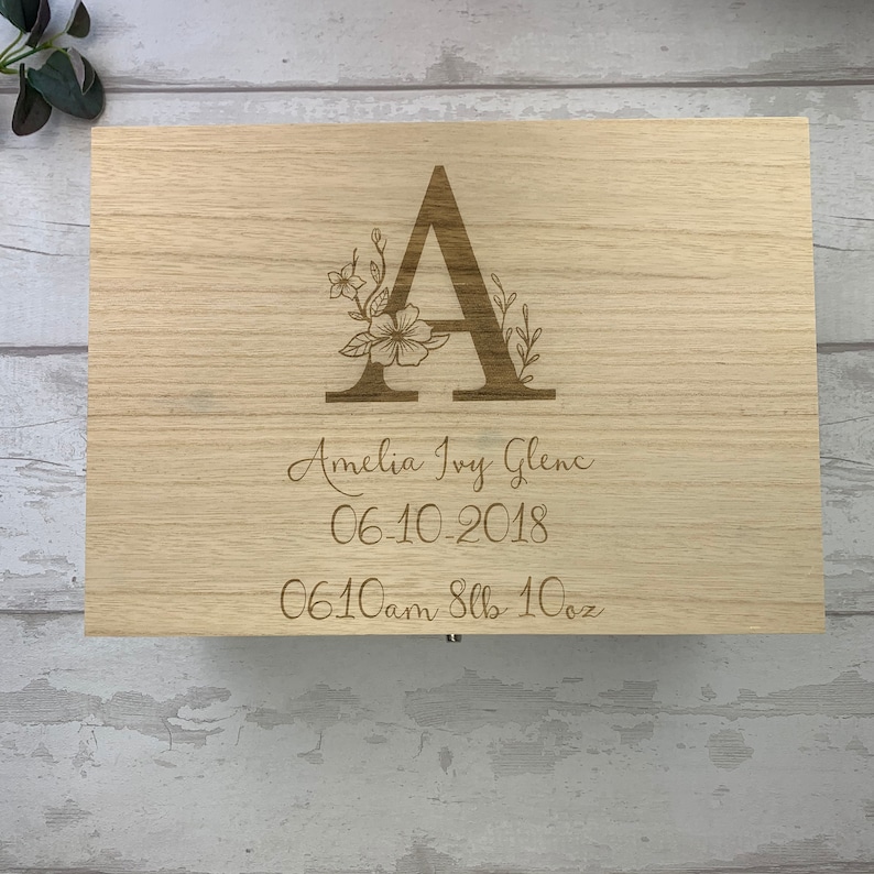 May include: A wooden keepsake box with an engraved floral design and the letter A. The box is personalized with the name Amelia Ivy Glens, the date 06-10-2018, and the time 06:10 am, 8 lbs 10 oz.