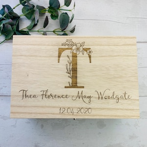 May include: A wooden box with a floral design and the letter "T" engraved on the front. The box also has the name "Thea Florence May Woodgate" and the date "12.04.2020" engraved on it.