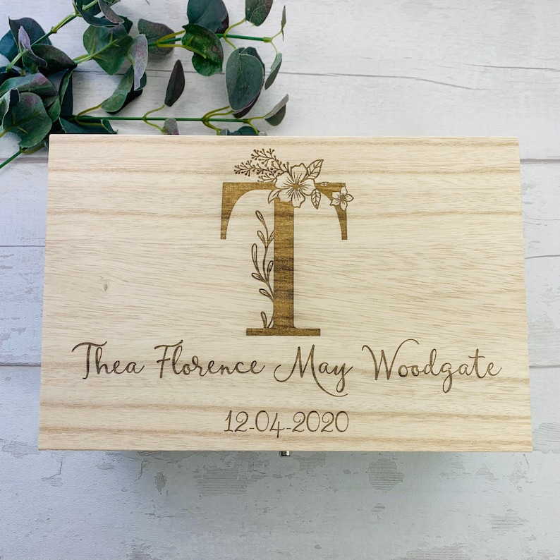 May include: A wooden box with a floral design and the letter "T" engraved on the front. The box also has the name "Thea Florence May Woodgate" and the date "12.04.2020" engraved on it.