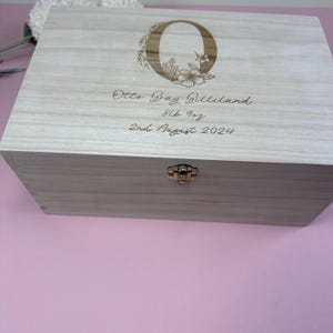 May include: A light wood keepsake box with a floral design and the letter "O" engraved on the lid. The box is engraved with the text "Otto Gray Gilliland 8lb 1oz 2nd August 2024".
