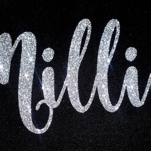 May include: Silver glitter name "Millie" in a cursive font on a black background.