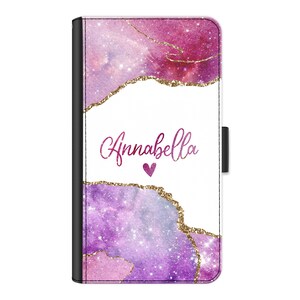 May include: A pink and purple galaxy-inspired phone case with gold glitter accents. The case has a white background with the name "Annabella" written in pink script and a small pink heart.