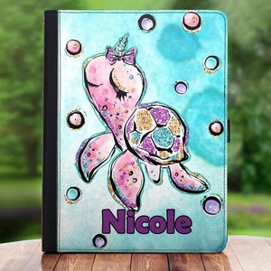 May include: A teal blue and pink tablet case featuring a unicorn sea turtle design. The turtle has a pink shell with gold and purple glitter accents. The case is personalised with the name "Nicole".