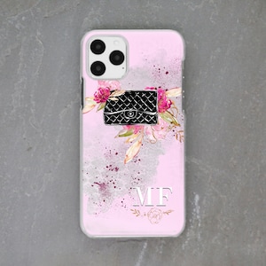 May include: A pink phone case featuring a black quilted handbag, pink flowers, and gold accents. The case has the initials "MF" printed on it.