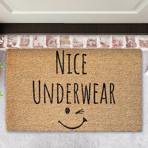 May include: A brown coir doormat with the text "NICE UNDERWEAR" in black lettering and a winking smiley face.