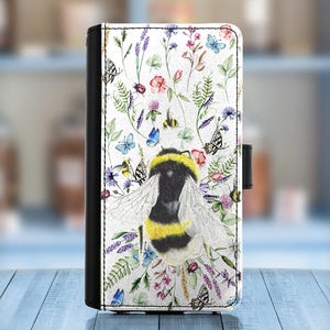 Puede incluir: Una funda de teléfono blanca con un diseño de acuarela de una abeja rodeada de flores y mariposas. La abeja es amarilla y negra con una raya blanca en la espalda.