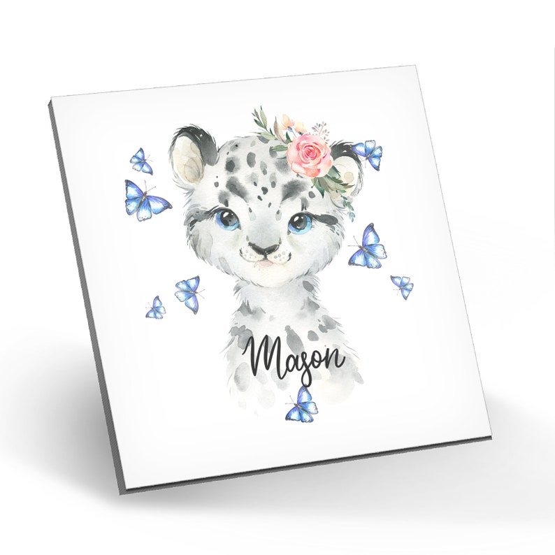 Puede incluir: Una ilustraci&oacute;n de acuarela de un lindo leopardo de las nieves con una corona de flores rosas y mariposas azules. El nombre "Mason" est&aacute; escrito debajo del leopardo de las nieves.