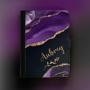 Peut inclure: &Eacute;tui pour tablette violet et noir avec des accents de paillettes dor&eacute;es et le nom Aubrey &eacute;crit en lettres dor&eacute;es. L'&eacute;tui est orn&eacute; d'un motif floral.