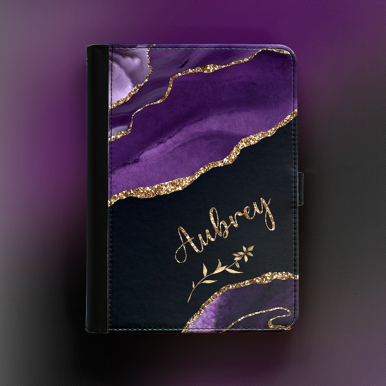 Peut inclure: &Eacute;tui pour tablette violet et noir avec des accents de paillettes dor&eacute;es et le nom Aubrey &eacute;crit en lettres dor&eacute;es. L'&eacute;tui est orn&eacute; d'un motif floral.