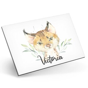 Puede incluir: Una ilustraci&oacute;n de acuarela de un lindo lince con hojas verdes detr&aacute;s. El nombre "Victoria" est&aacute; escrito en cursiva debajo del lince.