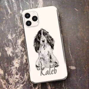 May include: Clear phone case featuring a watercolor-style illustration of a Cocker Spaniel dog in black and white. The dog's name, "Kaleb," is written in a script font at the bottom of the case. The phone case has a clear border.