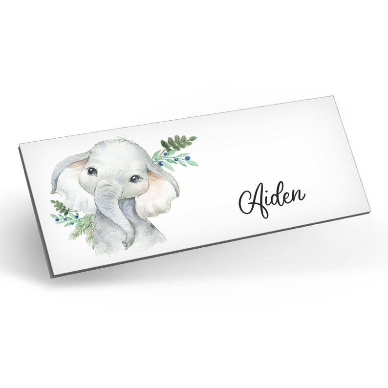 Puede incluir: Una ilustraci&oacute;n de acuarela de un lindo elefante gris con orejas rosadas y ojos azules. El elefante est&aacute; rodeado de hojas verdes y bayas azules. El nombre Aiden est&aacute; escrito en cursiva debajo del elefante.