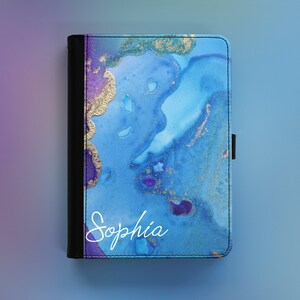 Peut inclure: Une housse pour liseuse avec un motif marbr&eacute; bleu et violet, des accents dor&eacute;s et le nom "Sophia" &eacute;crit en blanc.