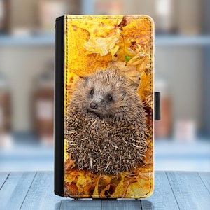 May include: A close-up of a hedgehog curled up in a ball of leaves. The hedgehog is brown and has a white belly. The leaves are yellow and orange.