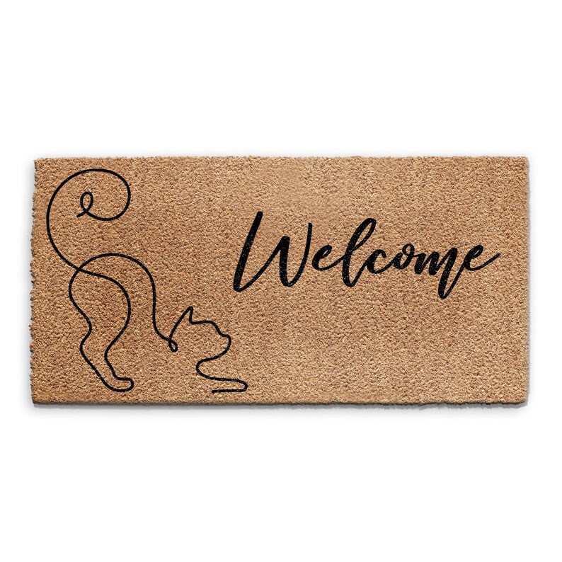 May include: A brown coir doormat with the word "Welcome" in black cursive lettering. A black line drawing of a cat is on the left side of the mat.