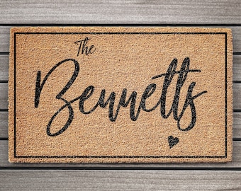 Puede incluir: Una alfombra de coco marrón con texto negro que dice "The Bennetts" y un pequeño corazón negro.