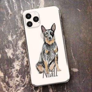 Könnte beinhalten: Eine weiße iPhone-Hülle mit einer Aquarell-Illustration eines sitzenden Blue Heeler Hundes. Der Name des Hundes, "Niall", ist in Schwarz unter dem Hund geschrieben.