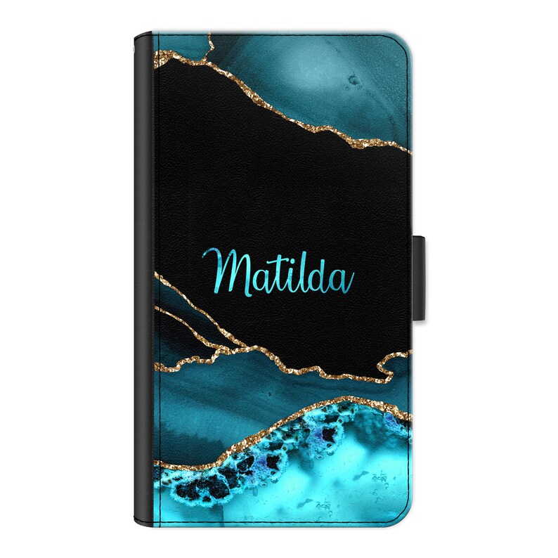 May include: A black phone case with a teal and gold abstract design. The name Matilda is written in teal on the case.