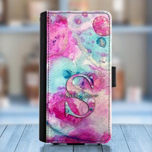 May include: A pink, blue, and white watercolor phone case with a black border and a silver letter "S" with the text "Sarah Jane" underneath.