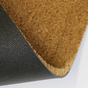 May include: Close-up of a brown coir doormat with a black rubber backing. The backing has a textured pattern.