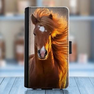 May include: A brown and white horse with a flowing mane runs through a field. The horse's mane is a bright orange color, and the horse's face is visible in the image. The horse is running towards the camera.