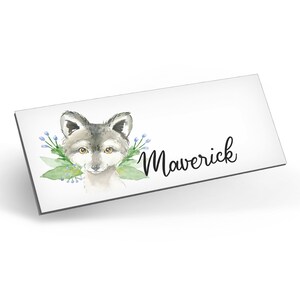 Puede incluir: Una ilustraci&oacute;n de acuarela de la cara de un lobo con flores azules y hojas verdes. El nombre "Maverick" est&aacute; escrito en cursiva debajo del lobo.