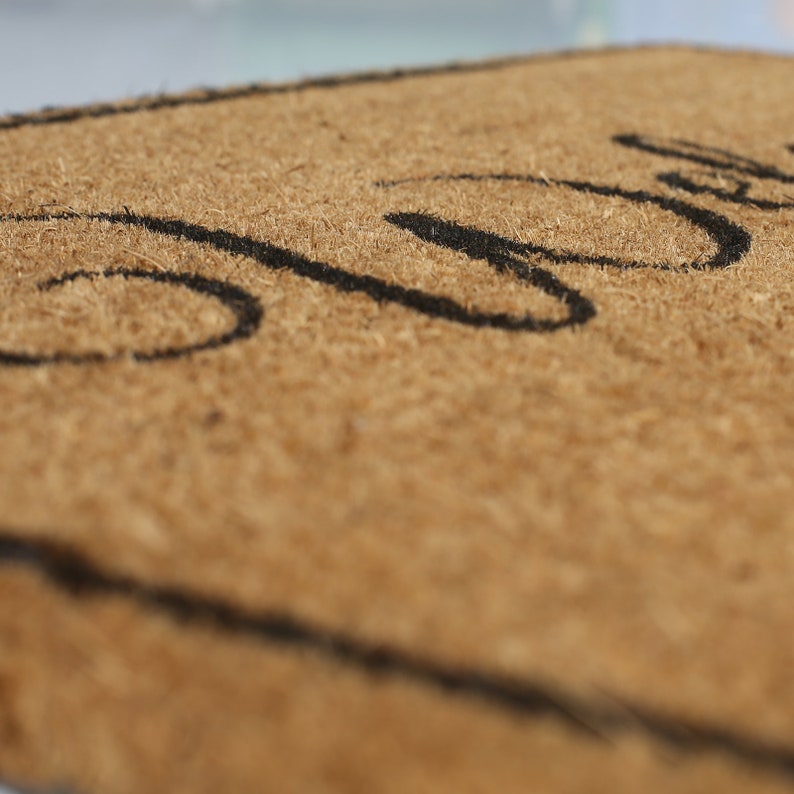May include: A brown coir doormat with the word "Welcome" written in black cursive lettering.