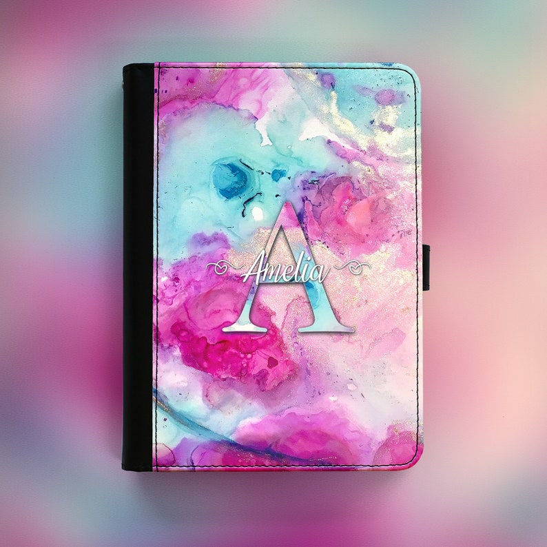 Peut inclure: Un design aquarelle rose, bleu et or avec une lettre A blanche et le nom Amelia en &eacute;criture cursive. Le design est sur une couverture en cuir noir.