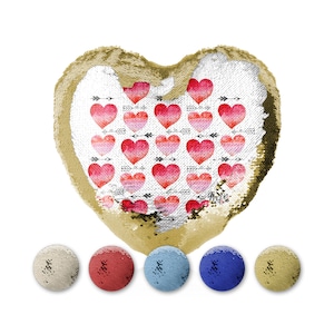 May include: A gold heart-shaped cushion with a reversible sequin design. One side features a white background with a pattern of pink and red watercolour hearts and black arrows. The other side is solid gold. The cushion is surrounded by four smaller round cushions in white, red, blue, and gold.