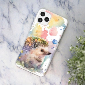 May include: A watercolor phone case featuring a colorful hedgehog with a white background and splashes of pink, yellow, blue, and green paint.
