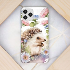 Puede incluir: Una ilustración de acuarela de un erizo con pelaje marrón y blanco, rodeado de flores rosas, azules y blancas. La ilustración está sobre un fondo blanco y es perfecta para una funda de teléfono.