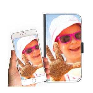 May include: A white phone case with a photo of a young girl wearing a pink hat and sunglasses, with her hand covered in sand. The girl is smiling and looking at the camera.