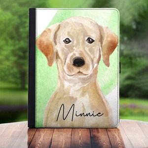 May include: A watercolor illustration of a yellow Labrador Retriever with the name "Minnie" written below. The dog is looking directly at the viewer with a soft expression. The background is a green and white watercolor wash.