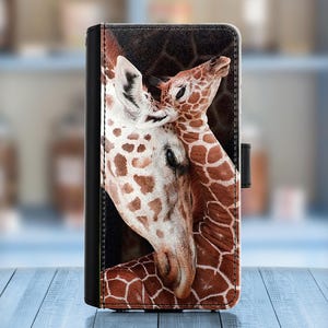 Puede incluir: Una funda de teléfono con una imagen de primer plano de dos jirafas, una con la cabeza apoyada en el cuello de la otra. Las jirafas tienen piel con patrones marrones y blancos.