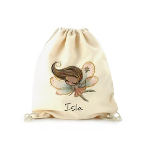 Op de afbeelding: Crèmekleurige trekkoordtas met een feeënillustratie. De fee heeft bruin haar, een roze jurk en gouden glitterdetails. De naam "Isla" is in zwart schrift gedrukt. De tas heeft een witte trekkoordsluiting.