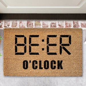 Può includere: Un tappetino per porta in fibra di cocco marrone con il testo "BEER O'CLOCK" in nero. La parola "BEER" è visualizzata in un font da orologio digitale.
