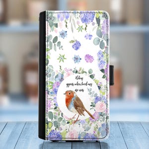 Può includere: Una custodia per telefono bianca con un design floreale e un pettirosso. Il testo "I pettirossi compaiono quando i cari sono vicini" è stampato sulla custodia.